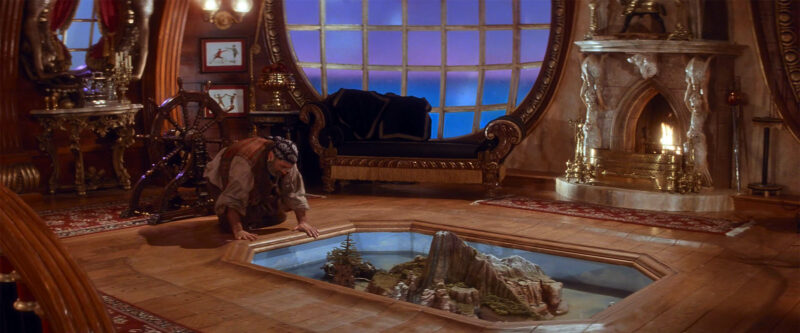 Smee gets down on his hands and knees to play with the miniature Neverland.